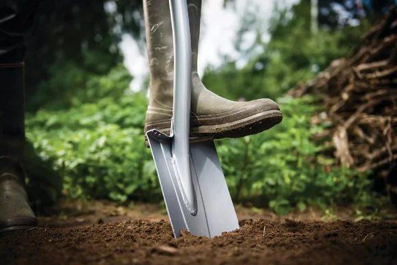 Person mit Stiefel gräbt mit Spaten Erde um